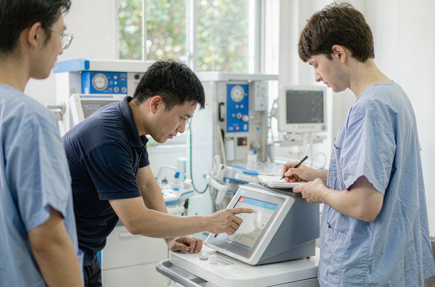 Service engineer training two veterinarians on a surgical device console in a clinic